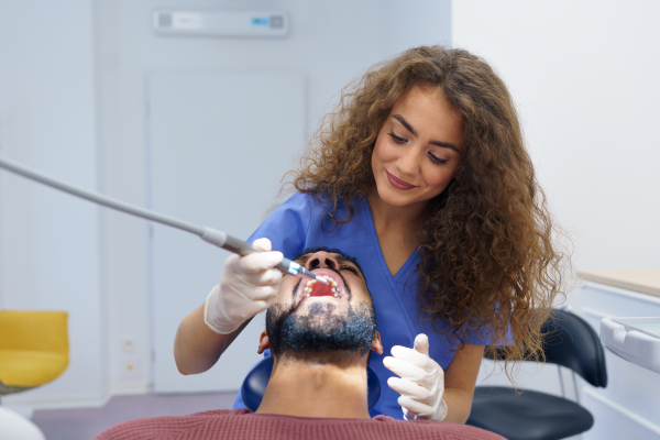 Young woman dentist doing preventive examination to the multiracial man.