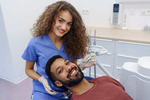 Young woman dentist doing doing preventive examination to the multiracial man.