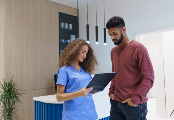 Young nurse talking with patient at reception in a private dental clinic.