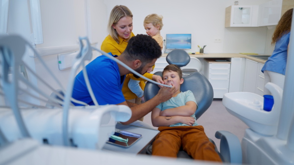 Little unhappy boy sitting in dentists chair, during the examination.