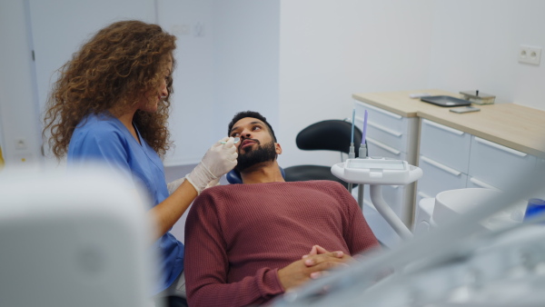 Young woman dentist doing doing preventive examination to the multiracial man.