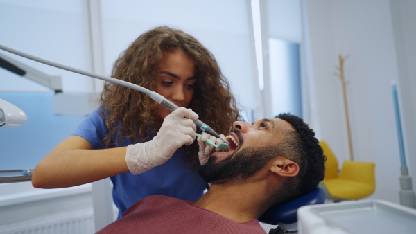 Young woman dentist doing doing preventive examination to the multiracial man.