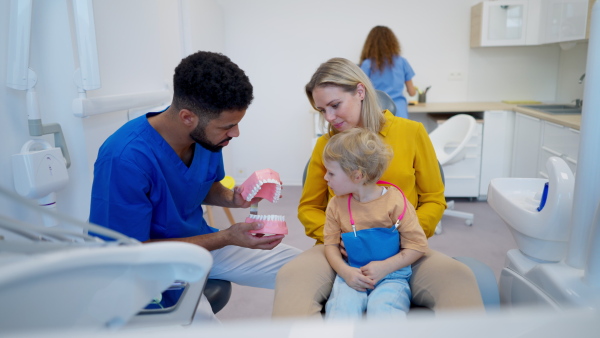 Young multiracial dentist showing a little girl how to clean teeth.