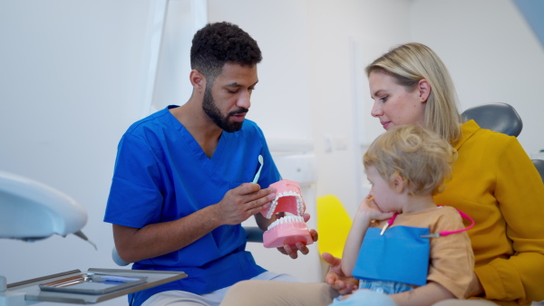 Young multiracial dentist showing a little girl how to clean teeth.