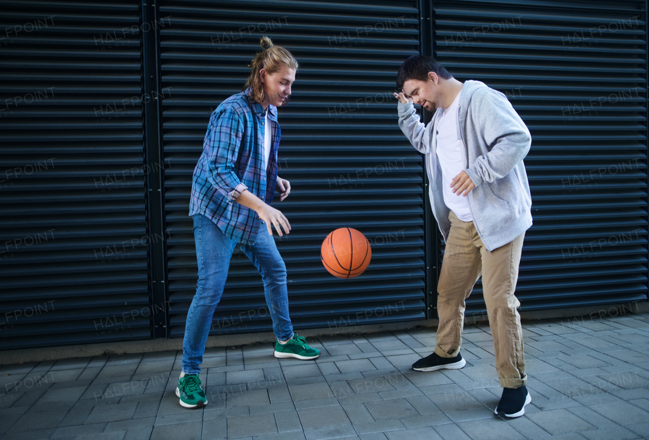 Man with down syndrome playing basketball outdoor with his friend. Concept of friendship and integration people with disability into the society.