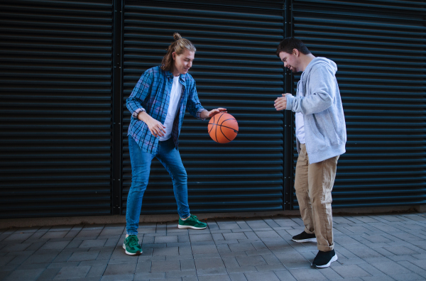 Man with down syndrome playing basketball outdoor with his friend. Concept of friendship and integration people with disability into the society.