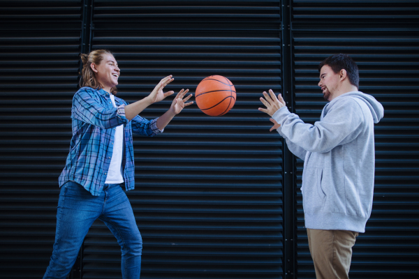 Man with down syndrome playing basketball outdoor with his friend. Concept of friendship and integration people with disability into the society.