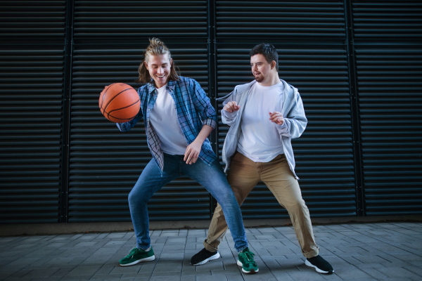 Man with down syndrome playing basketball outdoor with his friend. Concept of friendship and integration people with disability into the society.