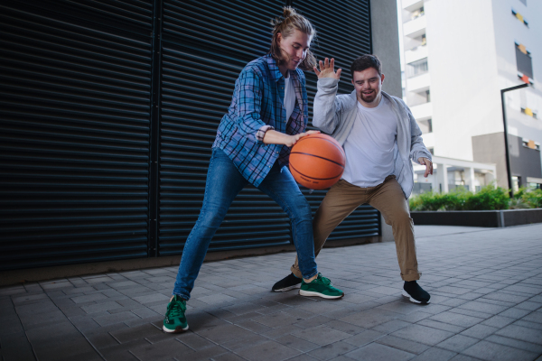 Man with down syndrome playing basketball outdoor with his friend. Concept of friendship and integration people with disability into the society.