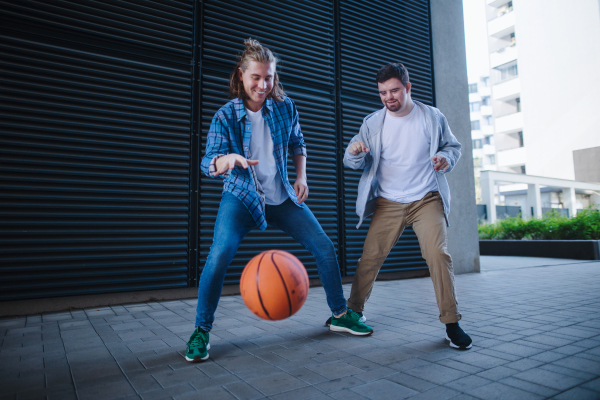 Man with down syndrome playing basketball outdoor with his friend. Concept of friendship and integration people with disability into the society.