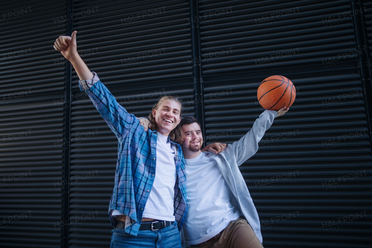 Man with down syndrome playing basketball outdoor with his friend. Concept of friendship and integration people with disability into the society.