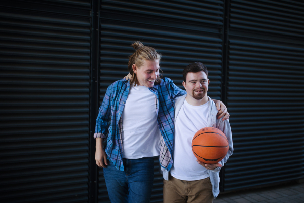 Man with down syndrome playing basketball outdoor with his friend. Concept of friendship and integration people with disability into the society.