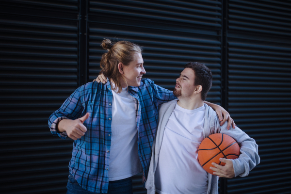 Man with down syndrome playing basketball outdoor with his friend. Concept of friendship and integration people with disability into the society.