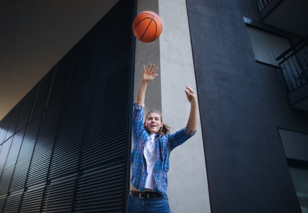 Young man throwing away a basketball ball,outdoor in city. Youth culture.