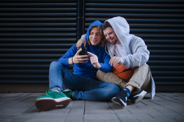 Man with down syndrome resting during basketball playing outdoor with his friend. Concept of friendship and integration people with disability into a society.