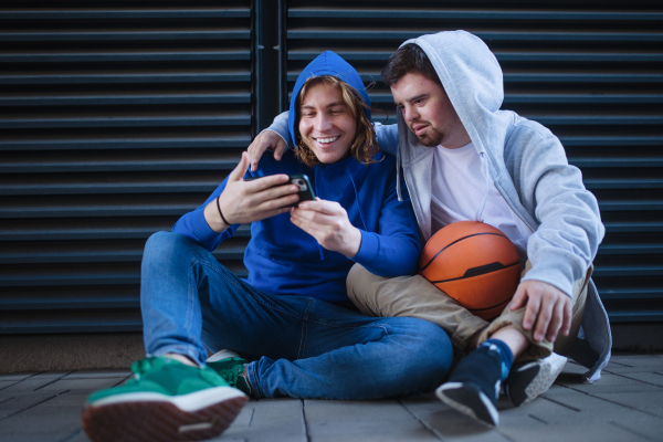 Man with down syndrome resting during basketball playing outdoor with his friend. Concept of friendship and integration people with disability into a society.