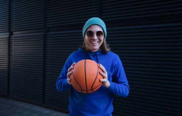 Portrait of young man with cap and sunglasses holding basketball ball,outdoor in a city. Youth culture.