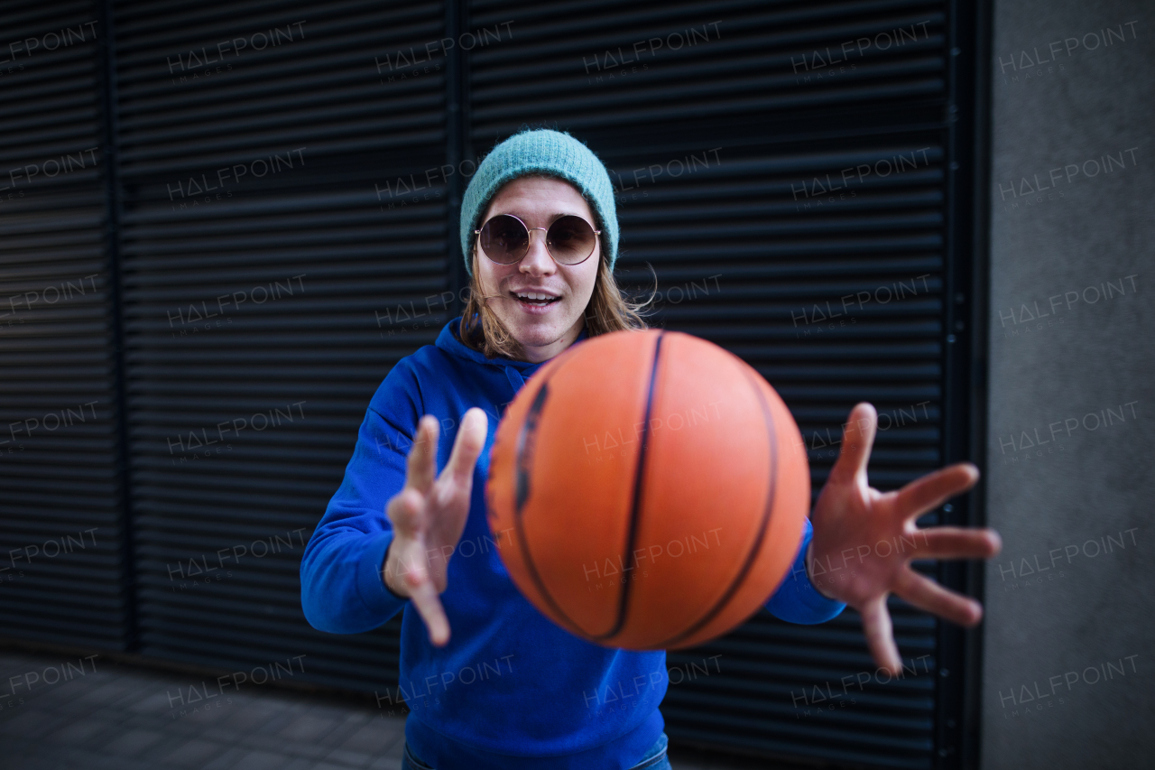 Portrait of young man with cap and sunglasses holding basketball ball,outdoor in a city. Youth culture.