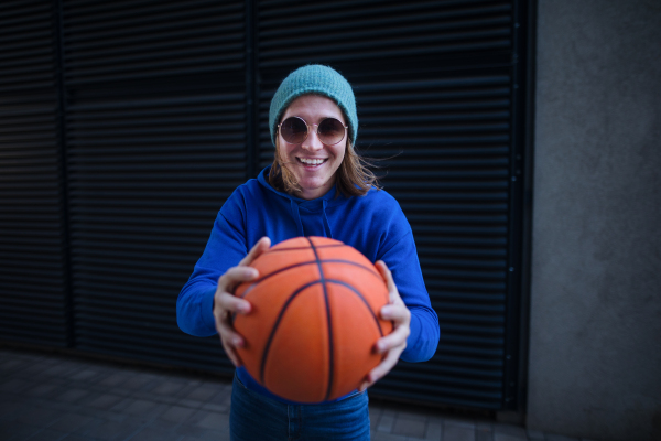 Portrait of young man with cap and sunglasses holding basketball ball,outdoor in a city. Youth culture.