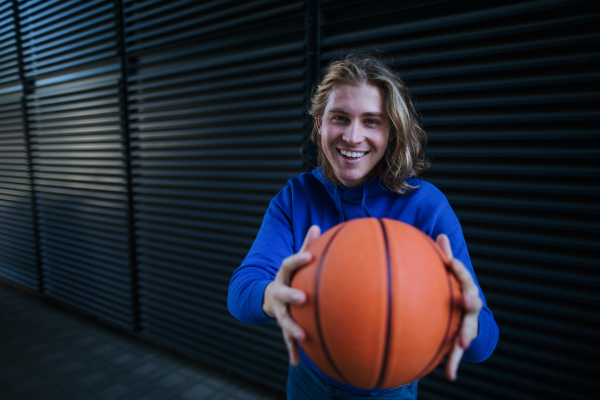 Portrait of young man with cap and sunglasses holding basketball ball,outdoor in a city. Youth culture.