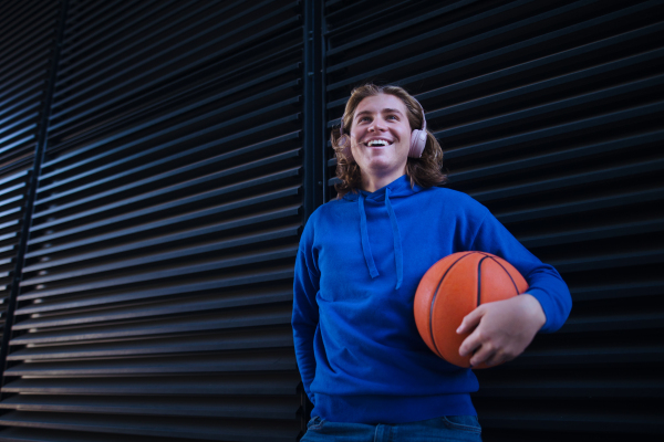 Portrait of young man with headphones holding basketball ball,outdoor in a city. Youth culture.