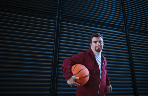 Portrait of young man with down syndrom holding a basketball ball.