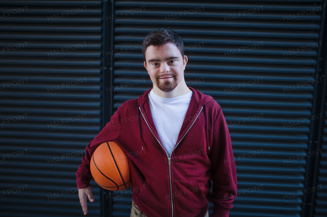 Portrait of young man with down syndrom holding a basketball ball.