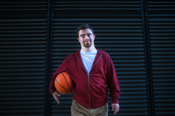 Portrait of young man with down syndrom holding a basketball ball.