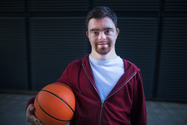 Portrait of young man with down syndrom holding a basketball ball.