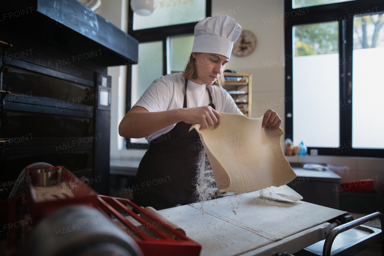 Young baker with chef cap preparing pastries in a bakery.