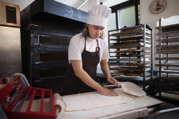 Young baker with chef cap preparing pastries in a bakery.