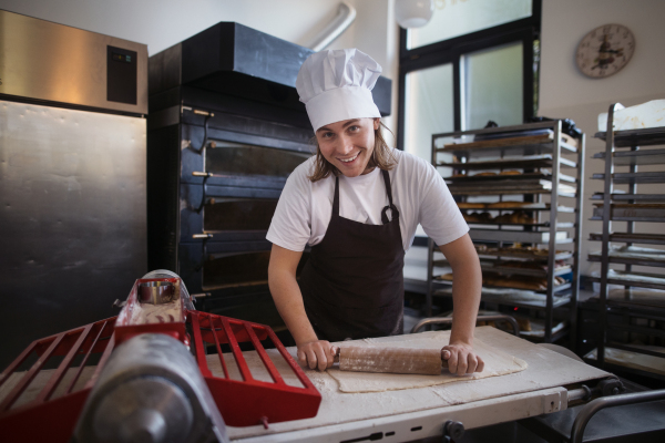 Young baker with chef cap preparing pastries in a bakery.