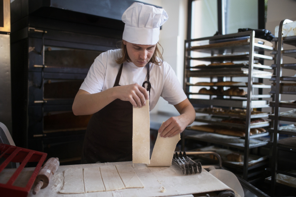 Young baker with chef cap preparing pastries in a bakery.