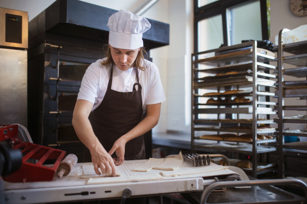 Young baker with chef cap preparing pastries in a bakery.