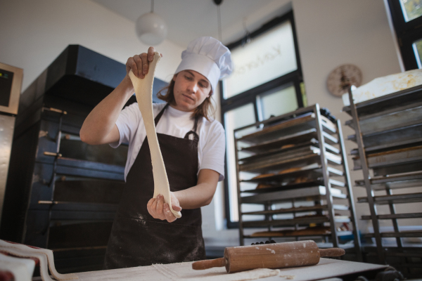 Young baker with chef cap preparing pastries in a bakery.