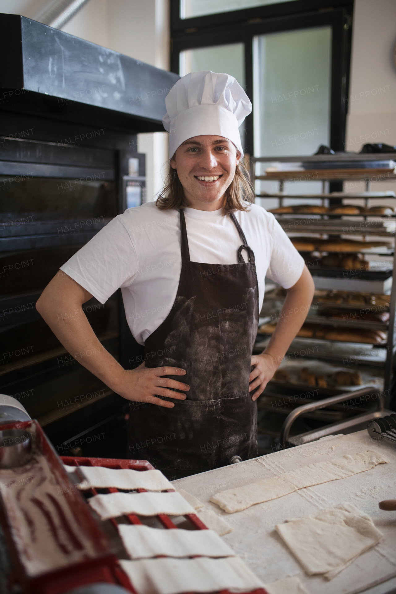 Young baker with chef cap preparing pastries in a bakery.