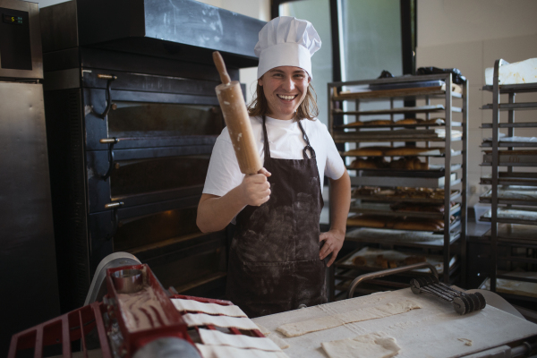 Young baker with chef cap preparing pastries in a bakery.