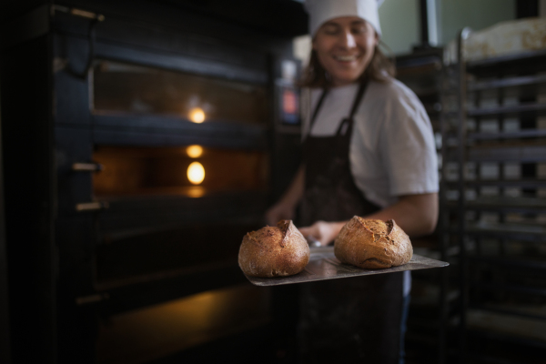 Happy young baker with fresh bread, in a bakery.