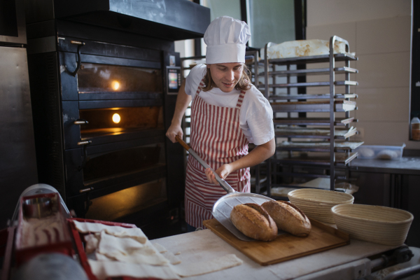 Happy young baker with fresh bread, in a bakery.