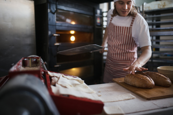 Happy young baker with fresh bread, in a bakery.