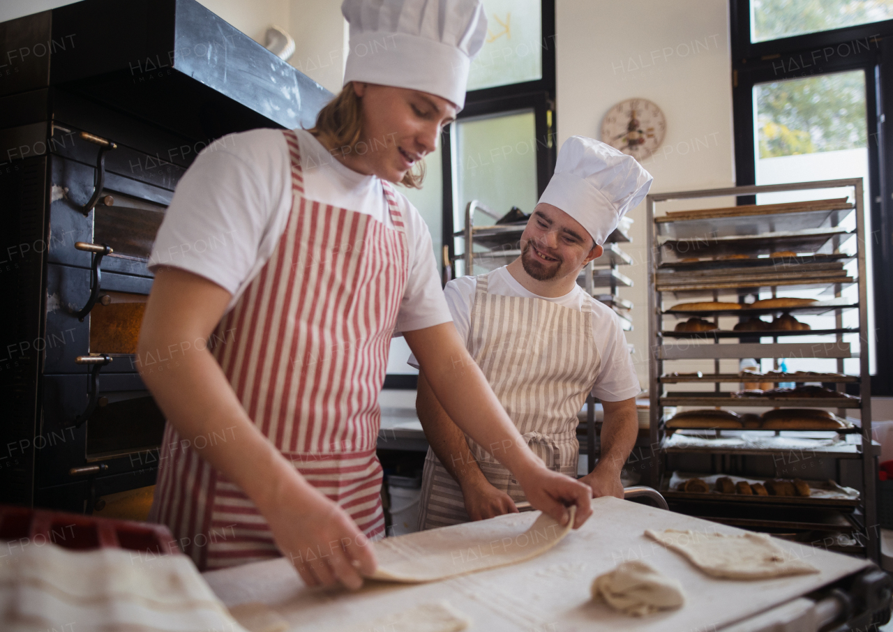 Man with down syndrom helping prepair bread in a bakery with his colleague. Concept of integration people with disability into society.