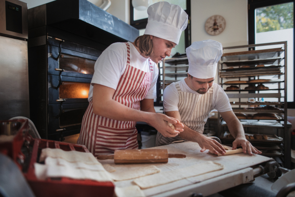 Man with down syndrom helping prepair bread in a bakery with his colleague. Concept of integration people with disability into society.