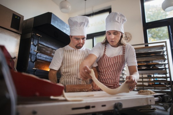 Man with down syndrom helping prepair bread in a bakery with his colleague. Concept of integration people with disability into society.