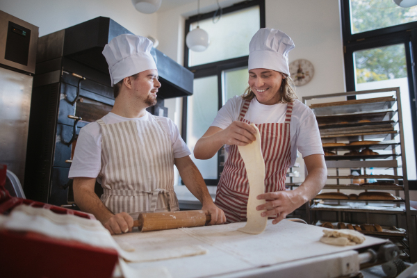 Man with down syndrom helping prepair bread in a bakery with his colleague. Concept of integration people with disability into society.