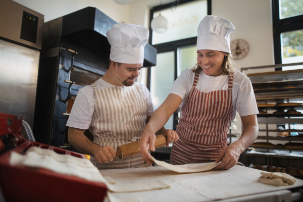 Man with down syndrom helping prepair bread in a bakery with his colleague. Concept of integration people with disability into society.