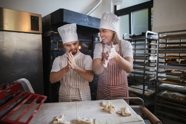 Man with down syndrom helping prepair bread in a bakery with his colleague. Concept of integration people with disability into society.