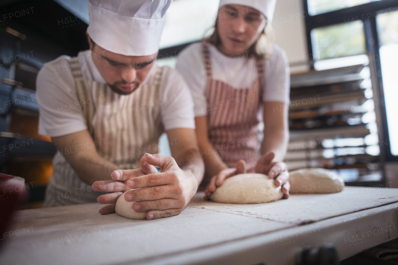 Man with down syndrom helping prepair bread in a bakery with his colleague. Concept of integration people with disability into society.