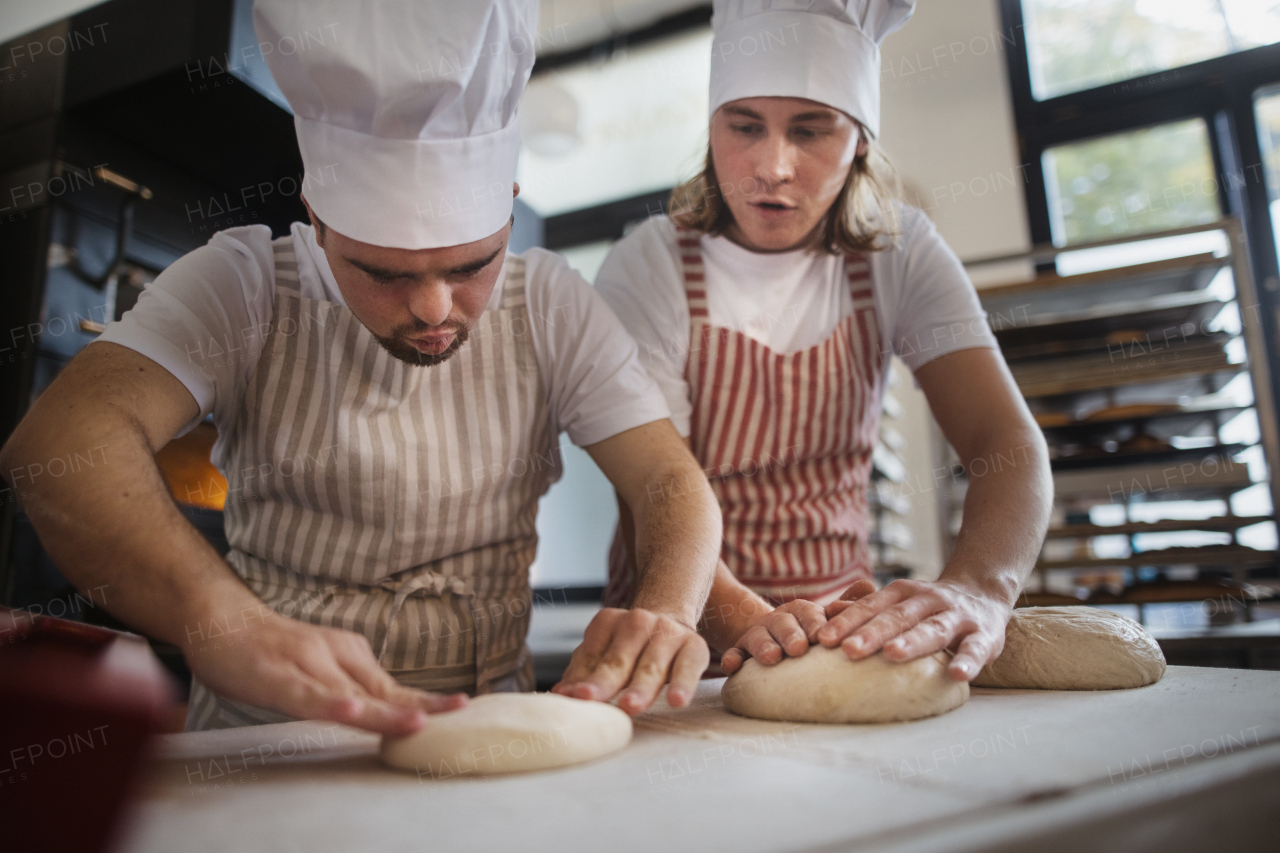 Man with down syndrom helping prepair bread in a bakery with his colleague. Concept of integration people with disability into society.