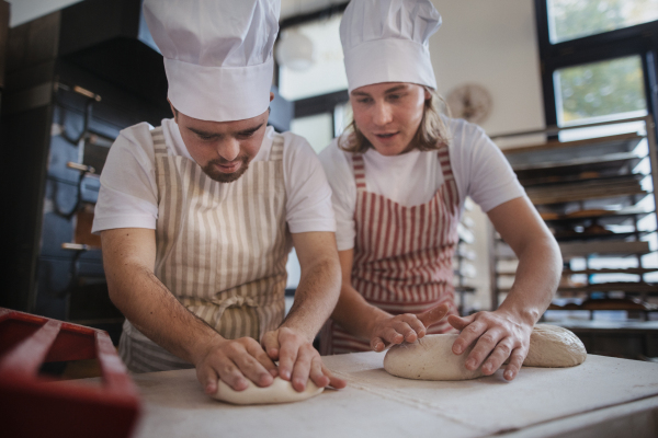 Man with down syndrom helping prepair bread in a bakery with his colleague. Concept of integration people with disability into society.