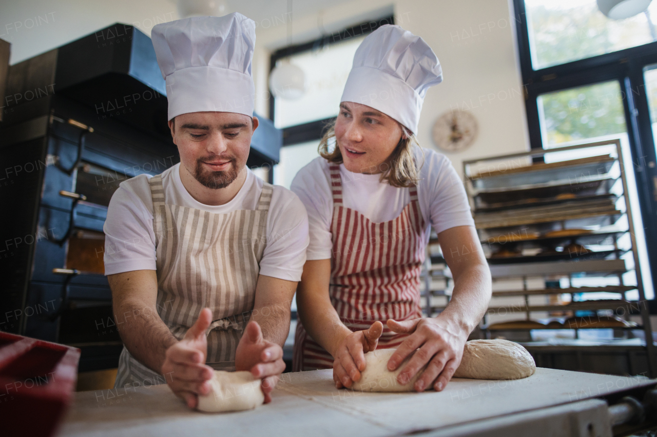 Man with down syndrom helping prepair bread in a bakery with his colleague. Concept of integration people with disability into society.